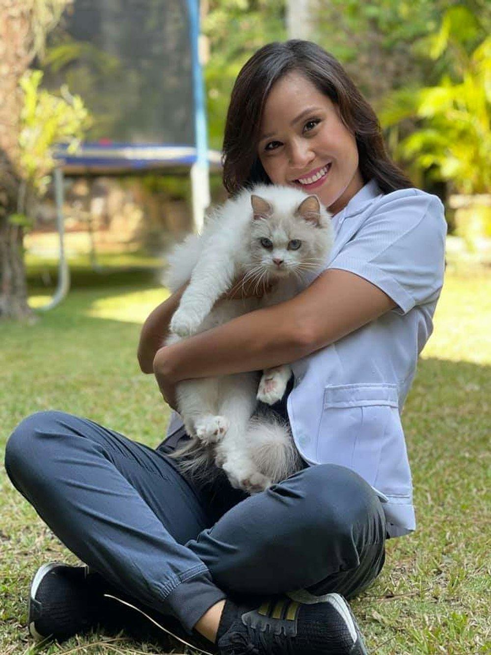 A smiling clinic team member sitting on the grass holding a fluffy white cat