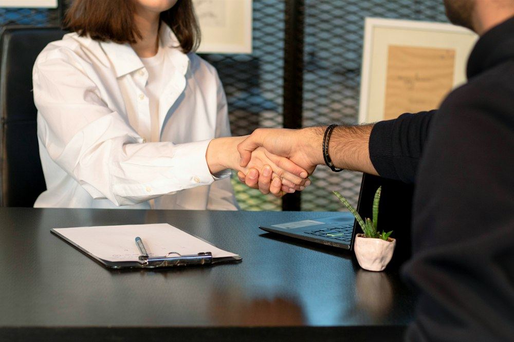 An owner and an associate shaking hands across a desk, with a clipboard between them