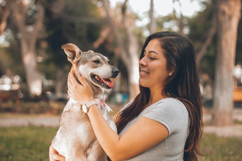 A woman smiling at her dog as she holds it up outdoors